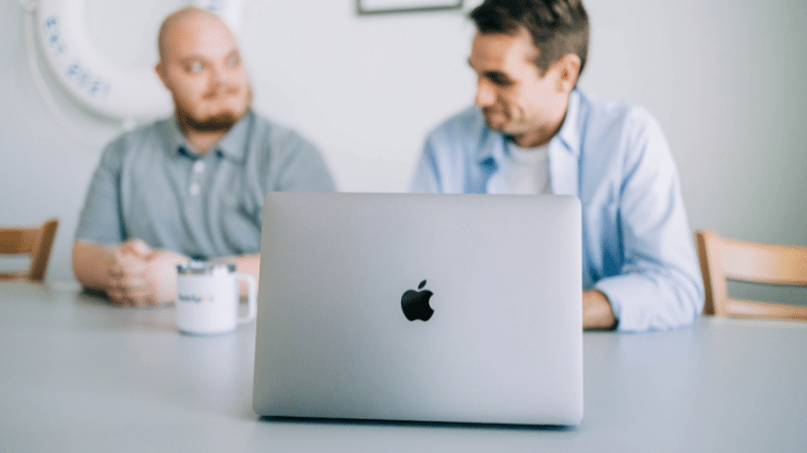 Two teammates at a table with a mug and laptop