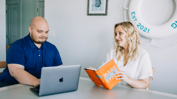 two coworkers at a table with a laptop and a book