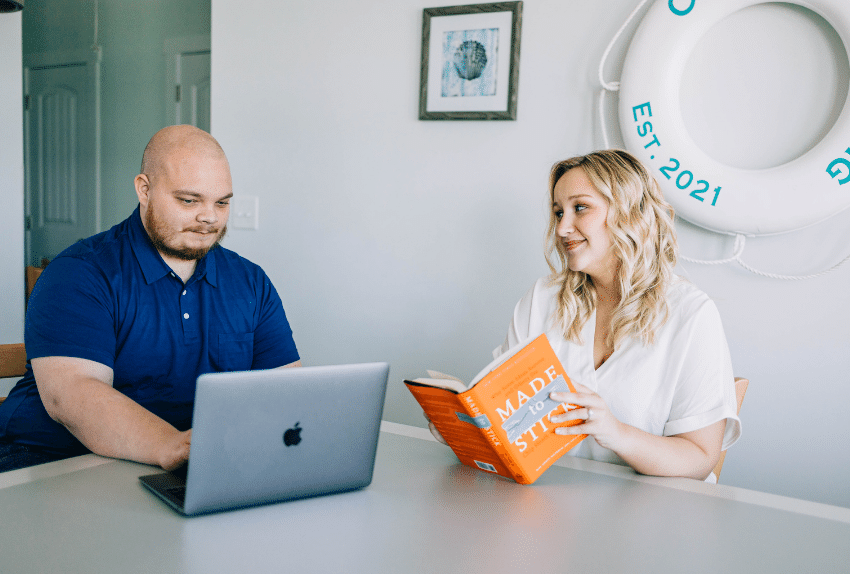 coworkers at table with laptop and book